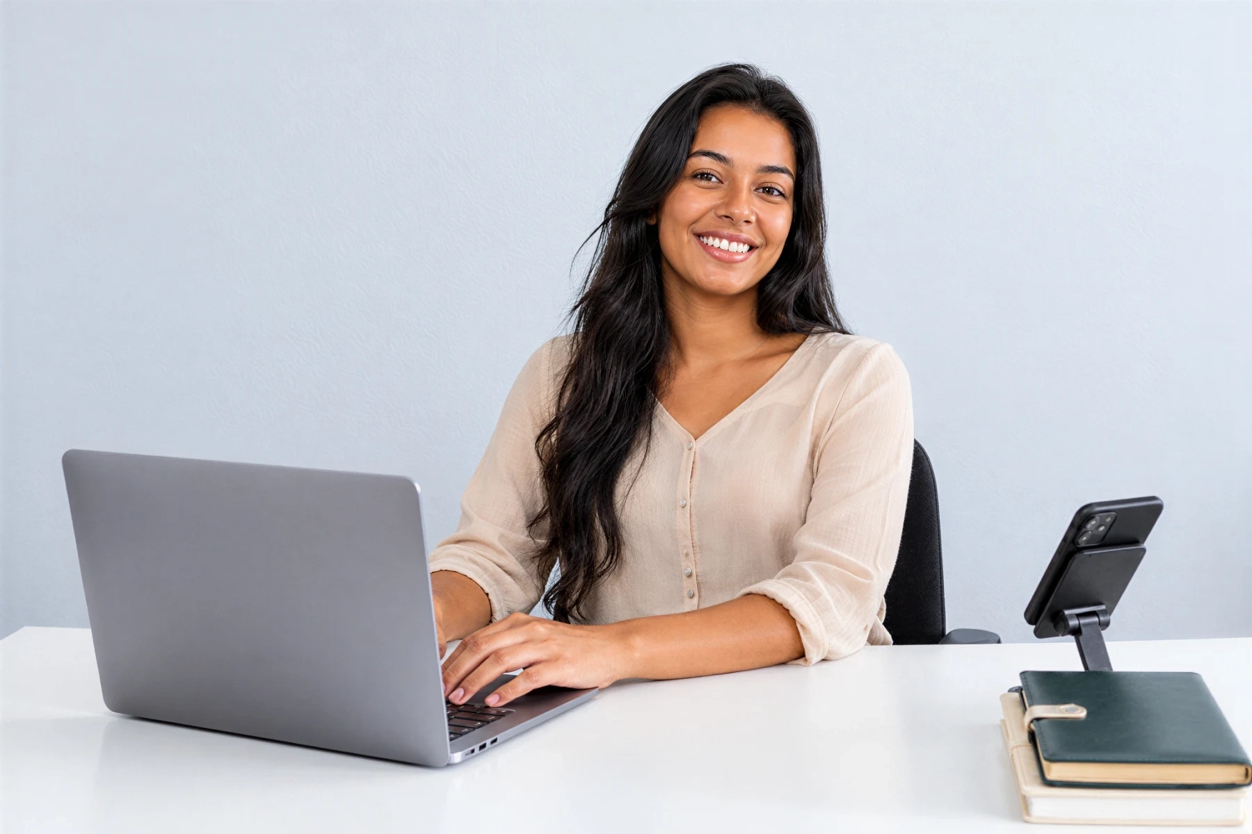 Joven profesional sonriente estudiando en su laptop en un escritorio con luz natural.